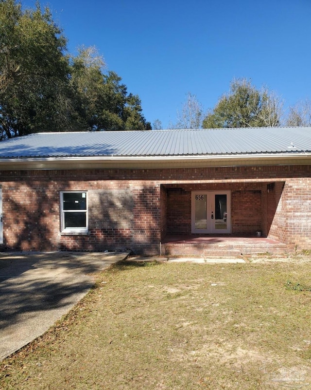 rear view of house featuring metal roof, french doors, brick siding, and a yard