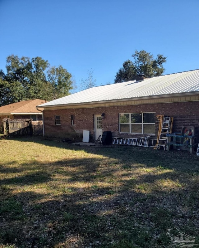 back of property featuring a lawn, metal roof, fence, and brick siding