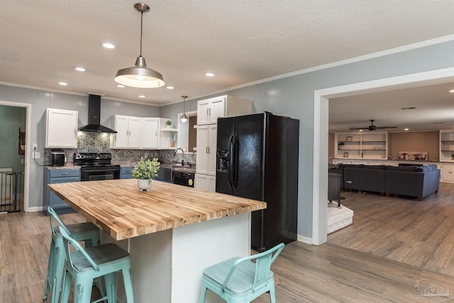 kitchen with wall chimney exhaust hood, wood counters, decorative light fixtures, black appliances, and white cabinetry