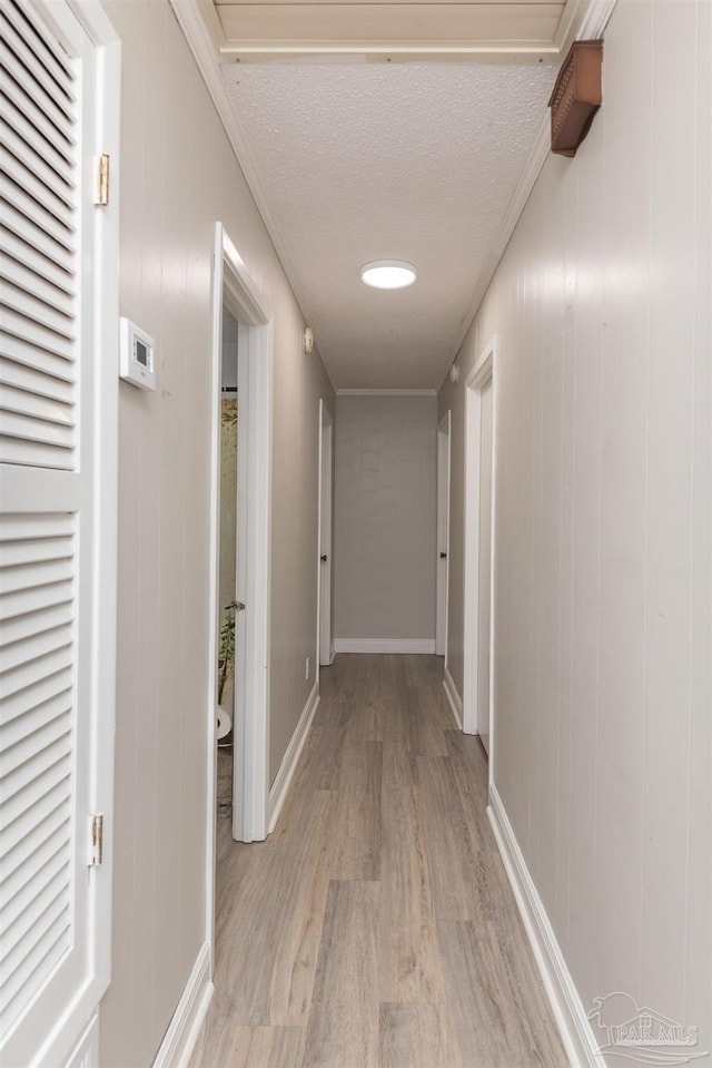 hall with a textured ceiling, crown molding, light wood-style flooring, and baseboards