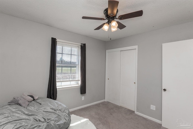 carpeted bedroom with a closet, ceiling fan, a textured ceiling, and baseboards