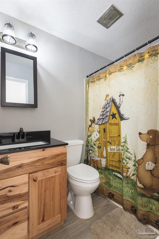 bathroom featuring visible vents, toilet, wood finished floors, a textured ceiling, and vanity