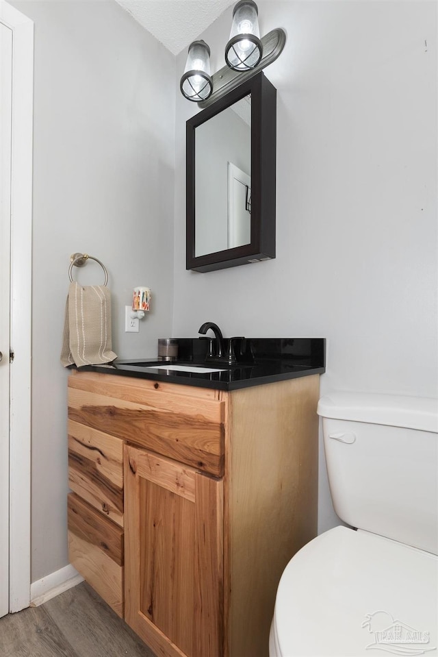 half bath featuring vanity, toilet, and wood finished floors