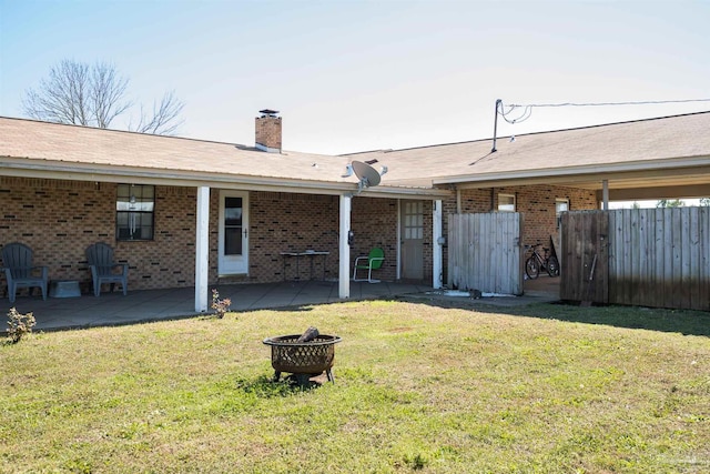 back of house featuring a fire pit, brick siding, fence, a lawn, and a chimney