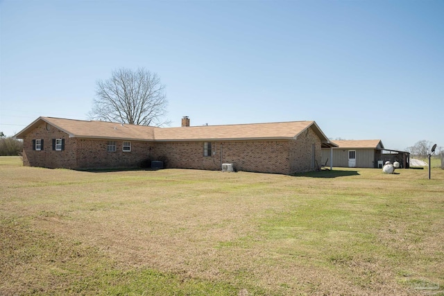 rear view of house with brick siding, a yard, a chimney, and central AC unit