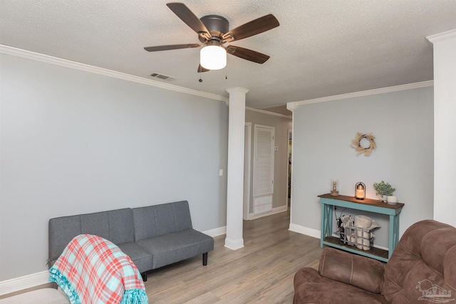 living room featuring a textured ceiling, wood finished floors, visible vents, decorative columns, and crown molding