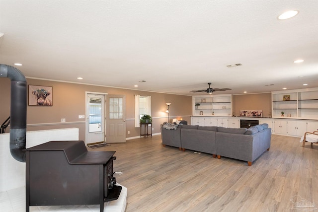 living area featuring a wood stove, ceiling fan, light wood-type flooring, and beverage cooler