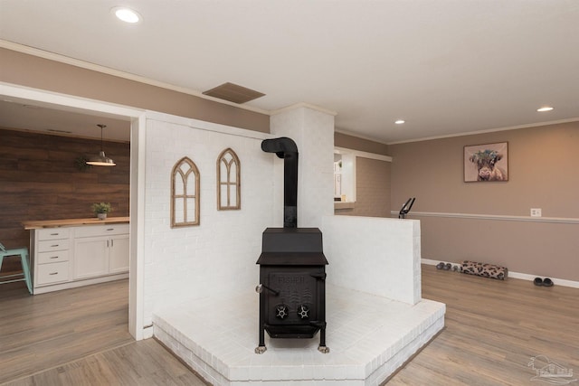 interior details featuring a wood stove, visible vents, wood finished floors, and ornamental molding