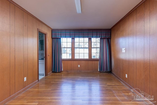 empty room with wood-type flooring, crown molding, and wooden walls