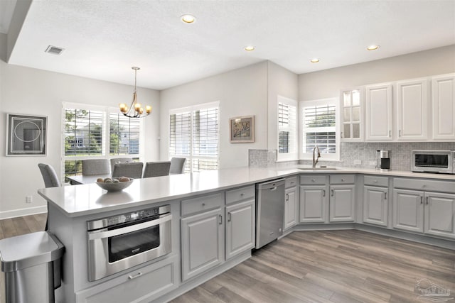 kitchen featuring appliances with stainless steel finishes, light hardwood / wood-style flooring, sink, decorative light fixtures, and a notable chandelier