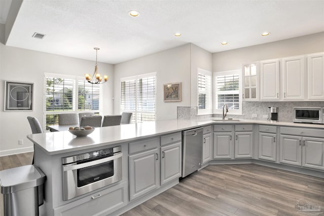 kitchen with sink, decorative light fixtures, appliances with stainless steel finishes, gray cabinets, and kitchen peninsula