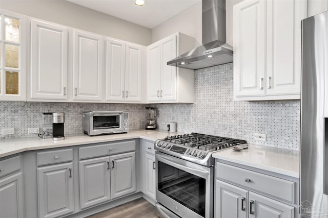 kitchen with wall chimney range hood, decorative backsplash, white cabinets, and appliances with stainless steel finishes