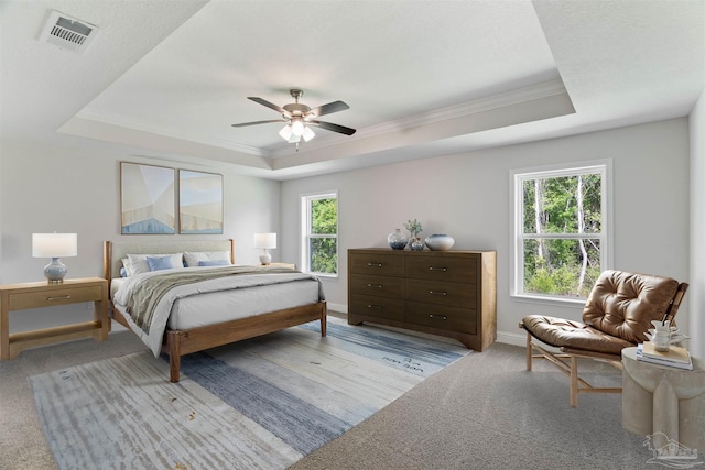 carpeted bedroom with baseboards, a raised ceiling, crown molding, and visible vents