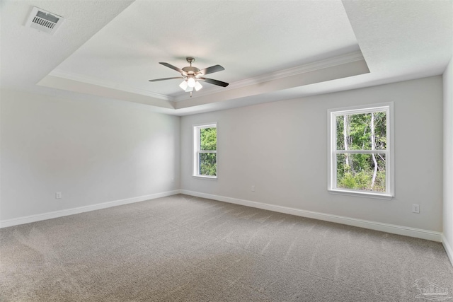 carpeted spare room with baseboards, crown molding, a tray ceiling, and visible vents