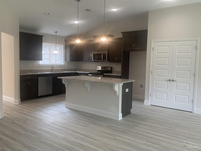 kitchen with a kitchen island, decorative light fixtures, light stone counters, stainless steel appliances, and light hardwood / wood-style flooring