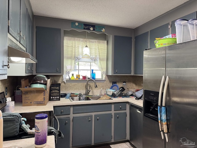 kitchen with stainless steel appliances, a sink, under cabinet range hood, light countertops, and a textured ceiling