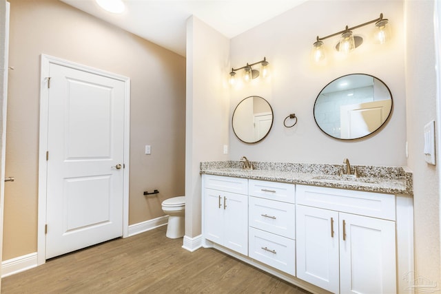 bathroom with toilet, double vanity, a sink, and wood finished floors