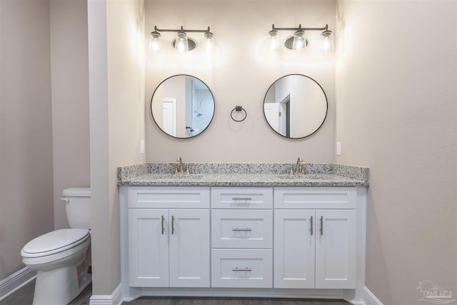 full bath featuring double vanity, a sink, toilet, and baseboards