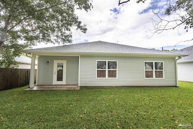 rear view of house with a yard, a shingled roof, and fence