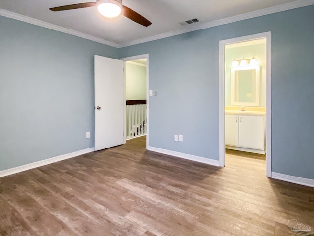 unfurnished bedroom featuring wood finished floors, a sink, visible vents, baseboards, and crown molding