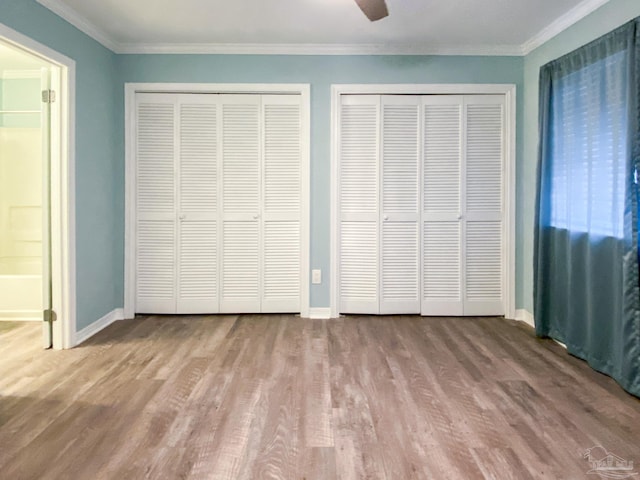 unfurnished bedroom with crown molding, multiple closets, a ceiling fan, wood finished floors, and baseboards