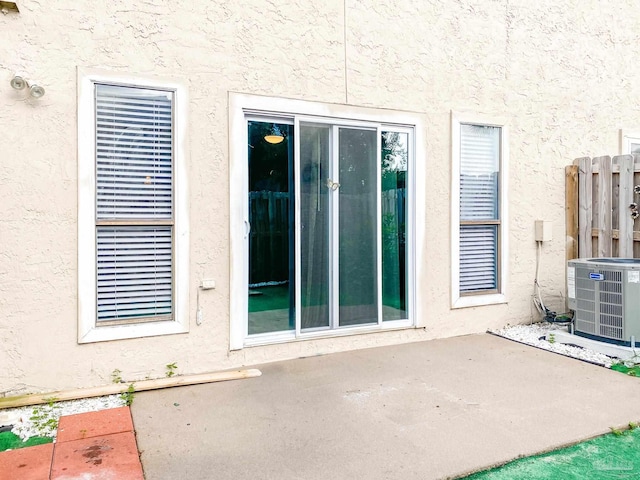 view of exterior entry featuring central AC unit, a patio, and stucco siding