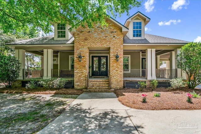 view of front of property featuring roof with shingles, covered porch, french doors, and brick siding