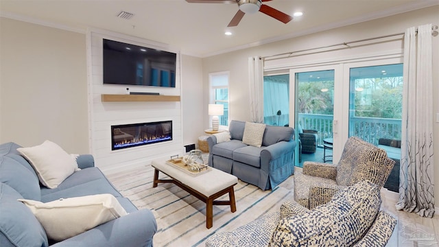 living room featuring ornamental molding, plenty of natural light, a large fireplace, and ceiling fan