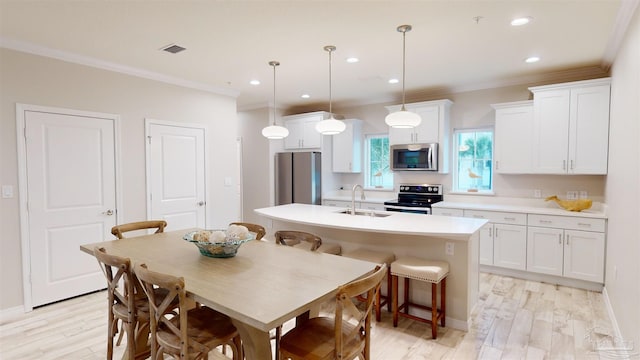 kitchen with sink, appliances with stainless steel finishes, an island with sink, pendant lighting, and white cabinets