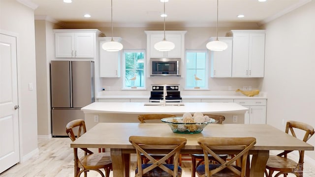 kitchen featuring pendant lighting, sink, white cabinets, stainless steel appliances, and a center island with sink