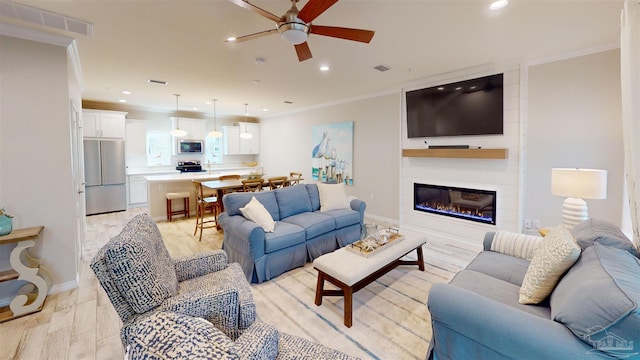 living room featuring ornamental molding, a large fireplace, ceiling fan, and light hardwood / wood-style flooring