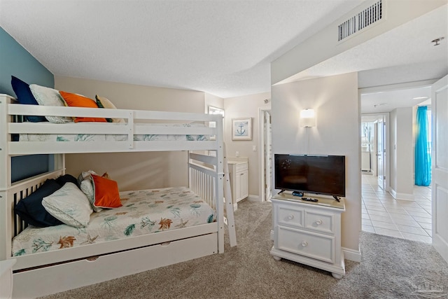 bedroom featuring a textured ceiling, ensuite bath, and light colored carpet