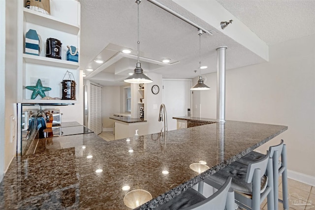 kitchen featuring hanging light fixtures, light tile patterned floors, a kitchen breakfast bar, a textured ceiling, and dark stone countertops