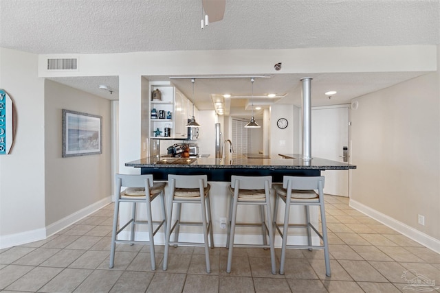 kitchen with a breakfast bar area, decorative light fixtures, a textured ceiling, and light tile patterned floors