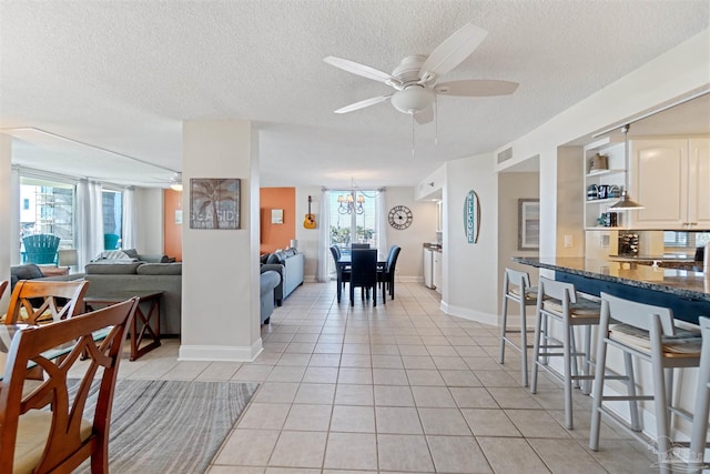 tiled dining space featuring a textured ceiling, plenty of natural light, and ceiling fan with notable chandelier