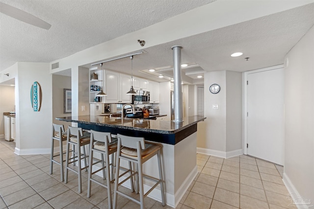 kitchen with white cabinets, appliances with stainless steel finishes, a textured ceiling, a kitchen bar, and pendant lighting