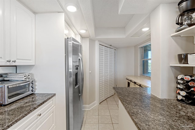 kitchen featuring stainless steel fridge, light tile patterned floors, white cabinetry, a textured ceiling, and dark stone counters