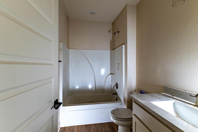 full bathroom featuring toilet, shower / tub combination, wood finished floors, a textured wall, and vanity