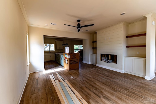 unfurnished living room with baseboards, dark wood-style flooring, ornamental molding, ceiling fan, and a large fireplace