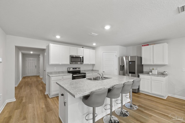 kitchen with stainless steel appliances, light countertops, light wood-type flooring, white cabinetry, and a sink