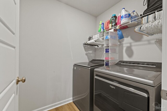 clothes washing area with laundry area, baseboards, washing machine and clothes dryer, and wood finished floors