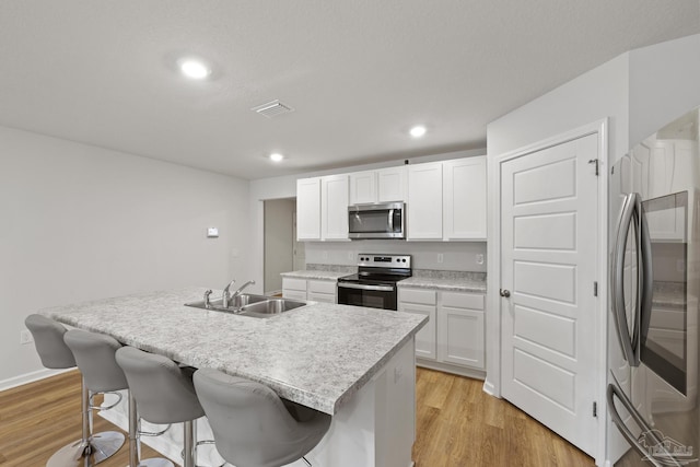 kitchen with light wood-type flooring, stainless steel appliances, a sink, and a kitchen breakfast bar