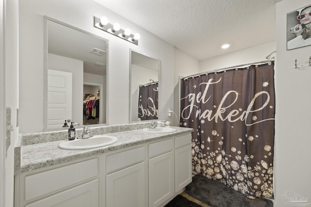 bathroom featuring visible vents, a sink, a textured ceiling, and double vanity