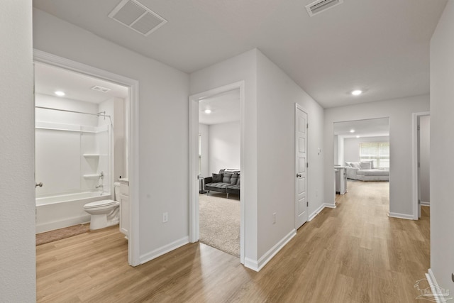 hall featuring light wood-type flooring, visible vents, and baseboards