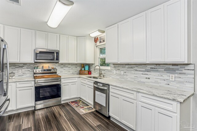 kitchen featuring stainless steel appliances, backsplash, white cabinetry, a sink, and dark wood-style flooring