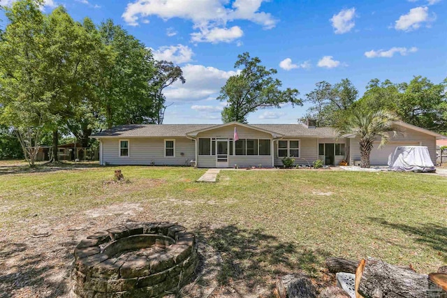 back of house featuring a garage, a sunroom, an outdoor fire pit, and a lawn
