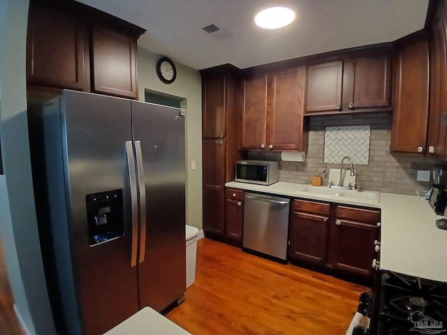 kitchen with dark brown cabinetry, tasteful backsplash, sink, light hardwood / wood-style flooring, and appliances with stainless steel finishes