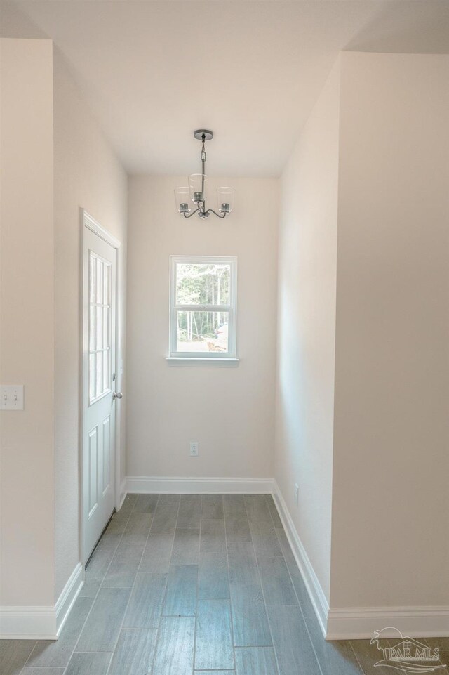 unfurnished dining area with baseboards, a notable chandelier, and wood finished floors