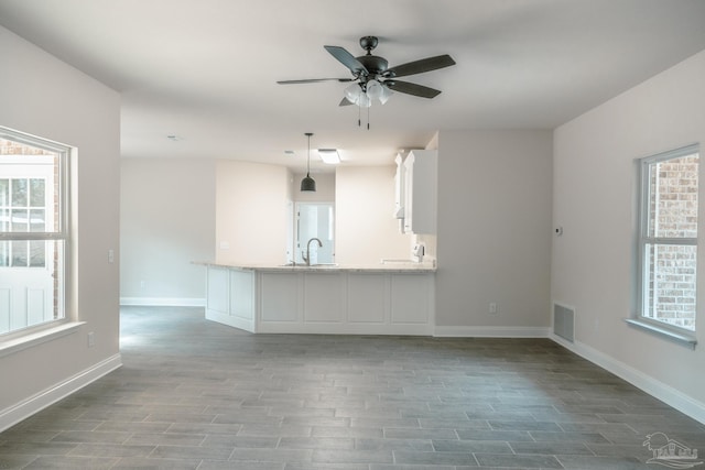 unfurnished living room with dark wood-style floors, visible vents, ceiling fan, a sink, and baseboards