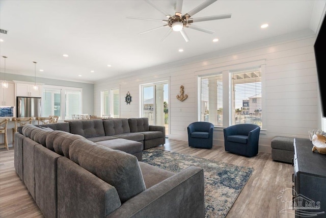 living room featuring ceiling fan, light hardwood / wood-style flooring, ornamental molding, and wooden walls